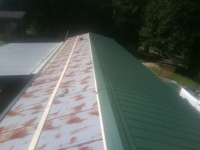 Old rusted panels beside newly installed green metal roofing — Wind Damage Roof Repair by Roofing Brothers in Montpelier